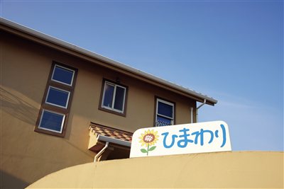 青空を背景にした、ひまわりの看板がある家（映画「ようこそ、ひまわりへ」メインビジュアル）